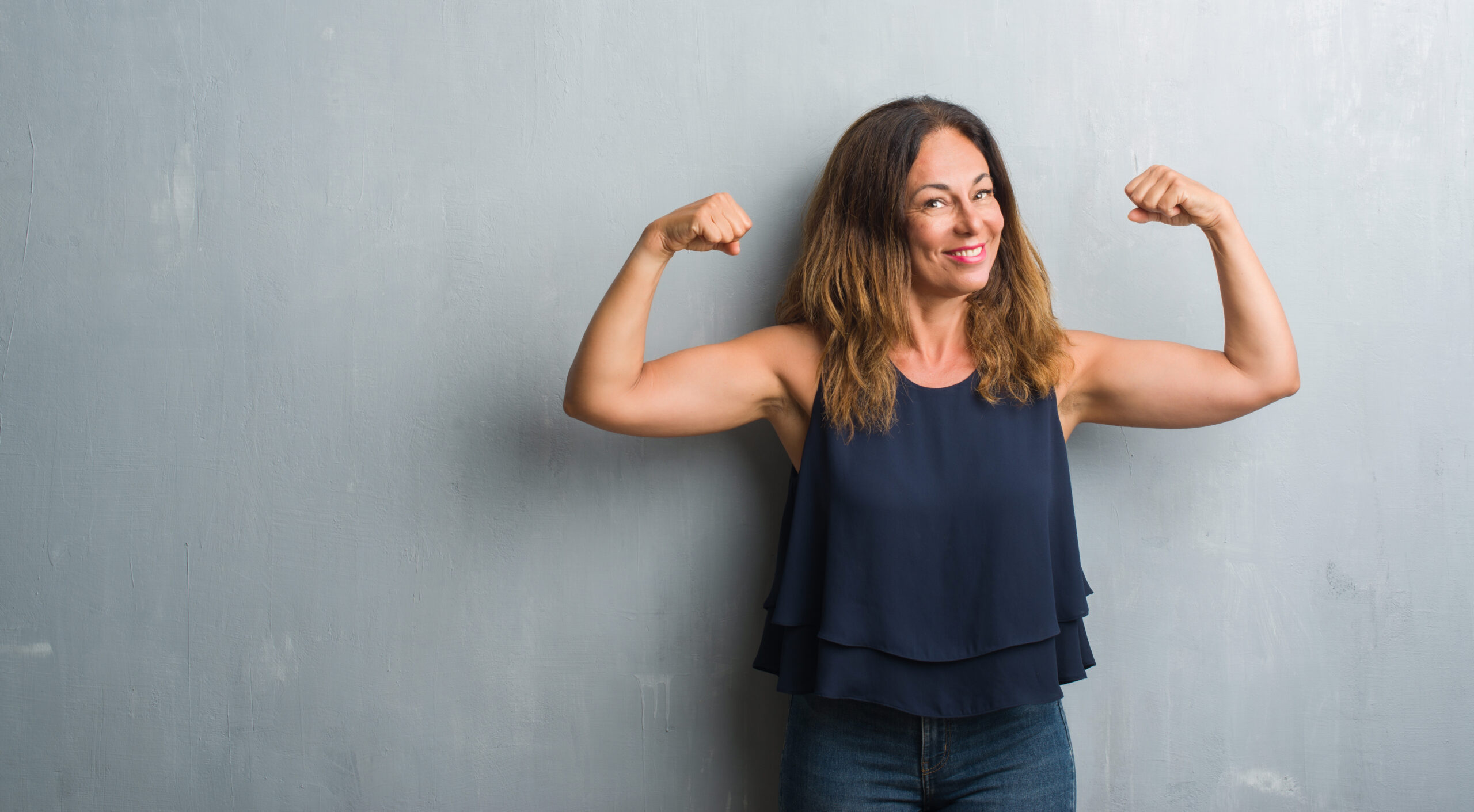 Woman flexing in front of a grey wall